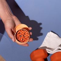 A hand holds an open orange pill tin filled with Golden Hour capsules at the gym.